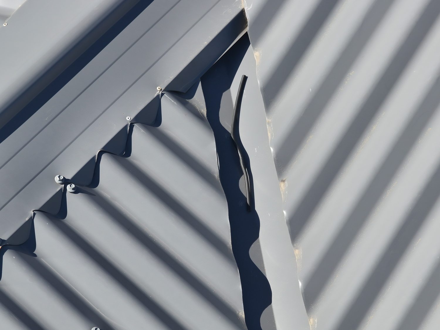 Redundant cut-off cable emerging from beneath hip capping and lying unsecured on the roof sheeting