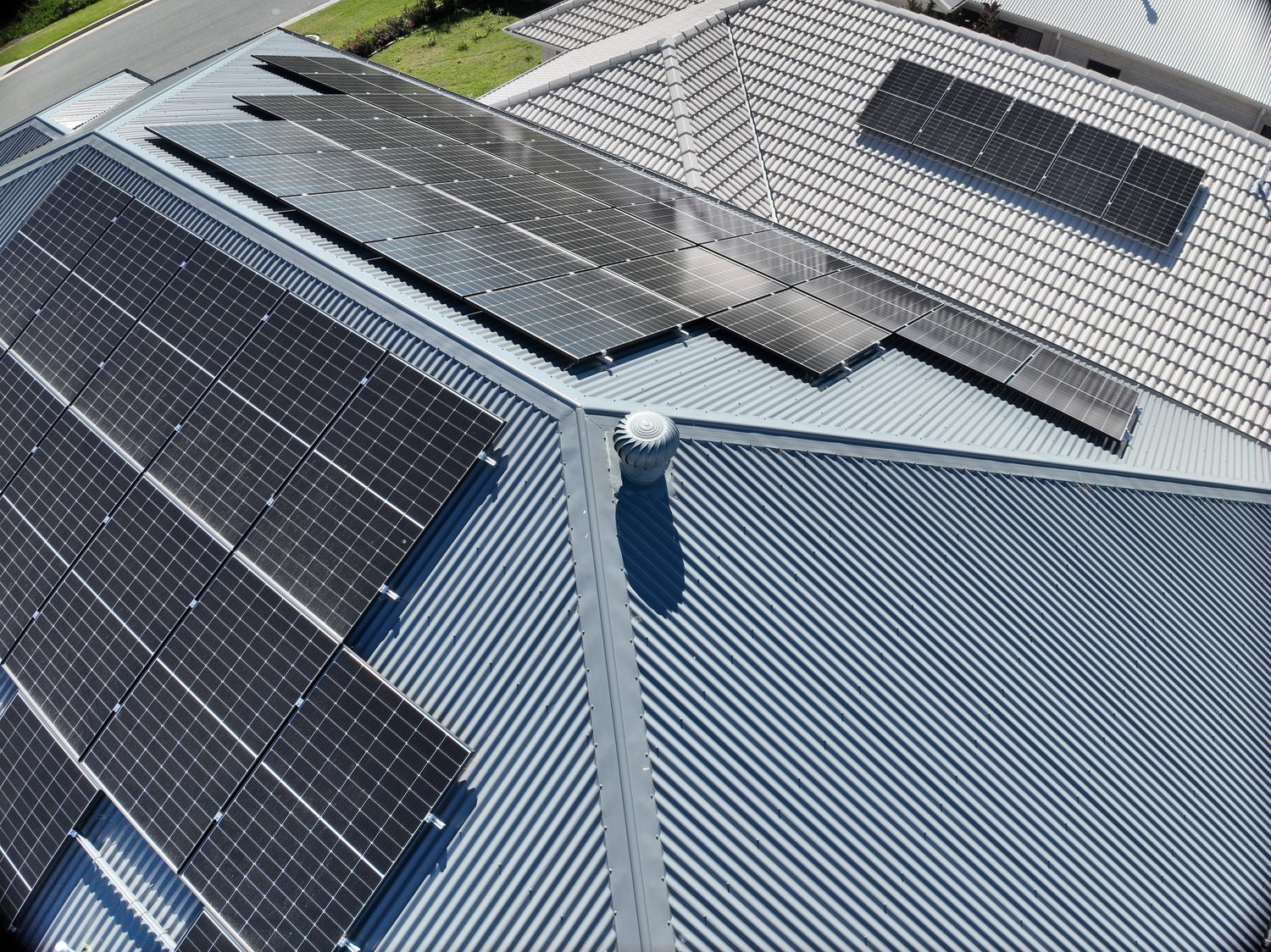 Drone inspection view of a metal hip-and-valley roof with rooftop solar arrays and a rotary ventilator